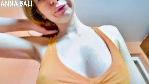 Anna Bali in seductive orange tank top, showing deep cleavage and slim figure