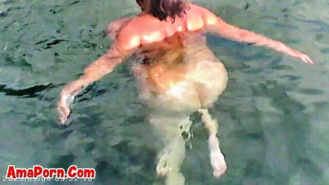Curvy brunette floating nude in clear tranquil waters, backside view
