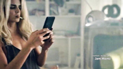Clara Lago in low-cut black dress, smoking cigarette while using phone, sexy cleavage view