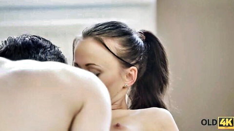 Petite brunette in ponytail passionately embraces nude older man