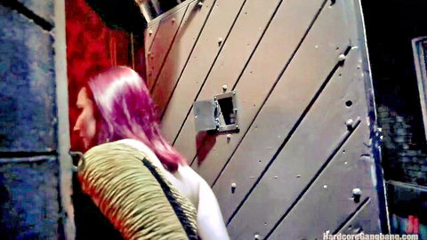 Pink-haired woman peeks through prison door in gangbang setup