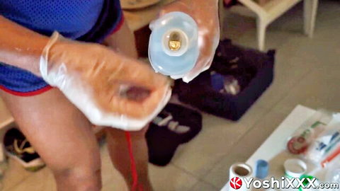 Gloved hands squeezing blue lube bottle over toned legs in tight blue shorts