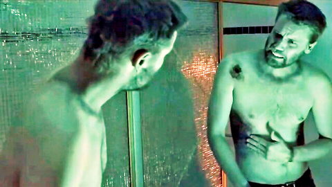 Muscular shirtless man with tattoos stares intensely in green-tinted bathroom mirror