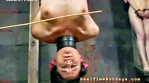 Asian woman bound and suspended upside down naked in BDSM scene with another nude model