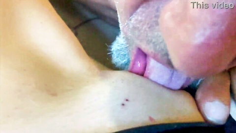 Bearded man with tongue out licking woman's pale neck and upper chest in closeup