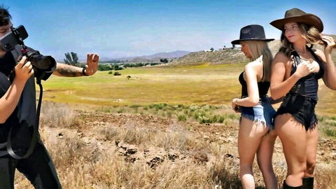 Two fit blondes in cowboy hats, denim shorts, and boots posing with big asses during outdoor influencer photo shoot