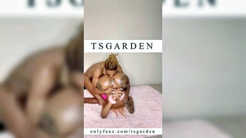 Busty ebony trans babe hugged from behind by muscular shemale, nude tits squeezed on pink rug