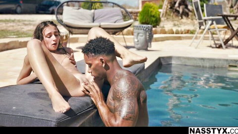 Skinny brunette teen spreads legs fingering wet pussy while tattooed black stud licks her foot poolside