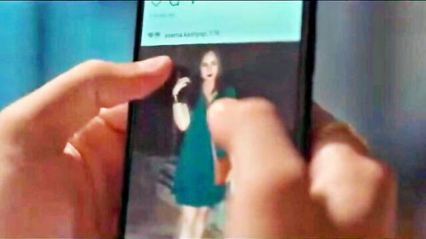 Hand holds phone displaying sexy South Asian babe in tight green dress with open mouth tease