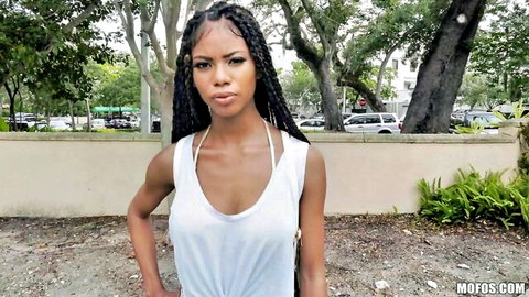 Nia Nacci in low-cut white tank top, posing outdoors with cleavage