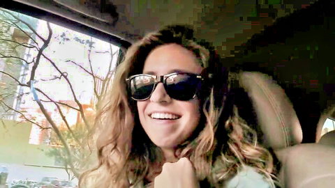 Smiling young woman with curly hair and sunglasses in car, amateur vibe