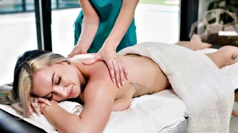 Tattooed blonde babe lies topless getting sensual back massage from sexy female masseuse