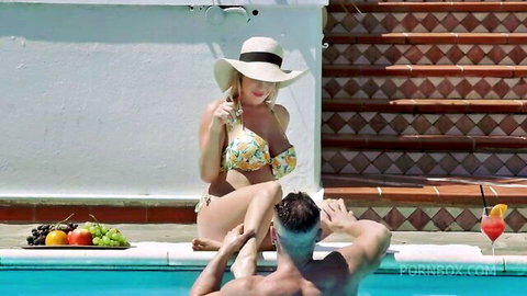 Blonde Marica in floral bikini lounging poolside with man in water, teasing threesome vibe