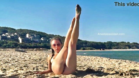Nude brunette woman in yoga pose exposing shaved pussy on public beach