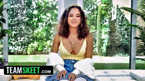 Curly-haired babe smiling with deep cleavage spilling from yellow top and tiny denim shorts