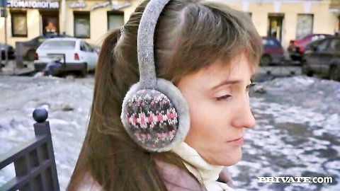 Slim Russian woman in winter earmuffs on snowy street, casting tease