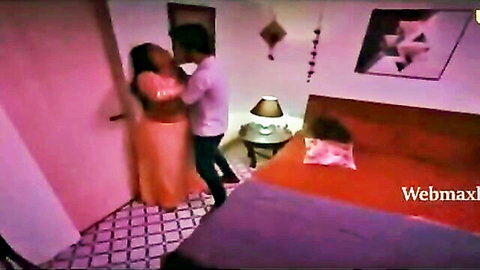 Indian couple passionately embracing in bedroom, woman in orange saree