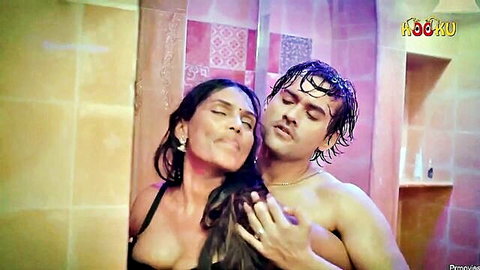 Busty Indian MILF in black bra passionately kisses wet muscular stud's neck grabbing his crotch in steamy bathroom