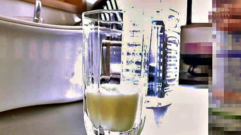 Thick yellow creamy liquid filling tall glass on kitchen counter in JAV scene