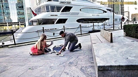 Blonde big tits babe in skimpy pink hotpants teases cleavage sitting on pier with kneeling boyfriend by luxury yacht