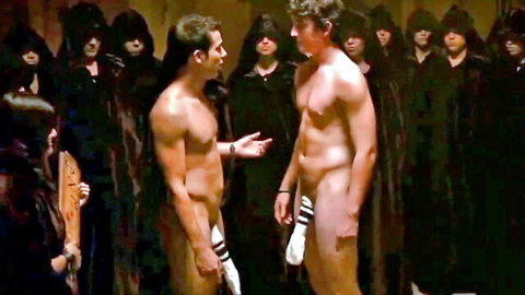 Two nude muscular men with exposed cocks stand before hooded cult figures in ritual scene