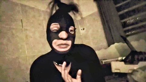 Gay man in shiny black latex mask with ponytail poses seductively in bathroom