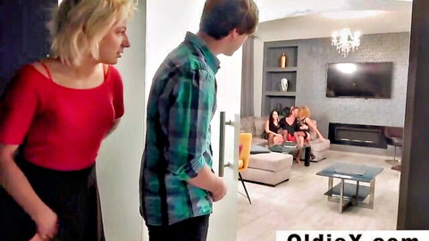 Blonde in red top at door with man, brunette women in dresses on couch