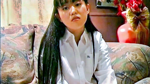 Cute Asian girl with long black hair and bangs pouting in white collared shirt on floral couch