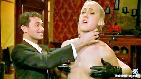 Suited dom in gloves chokes naked blonde sub's neck and gropes chest in BDSM dungeon