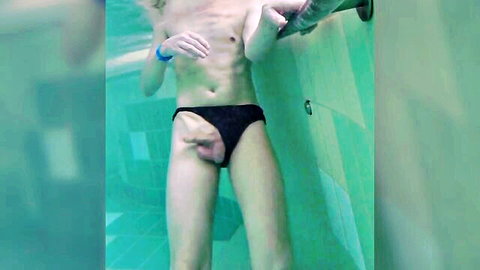 Slim young blond man in black speedo with visible bulge underwater in pool