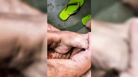 Blurry close-up of tan female feet in green flip-flops, held by hairy male hands for worship