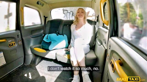 Blonde in white dress seated in Fake Taxi backseat, innocent pose