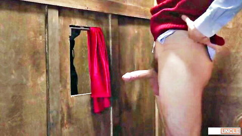 Man pulls down pants exposing hard erect cock near glory hole with red towel