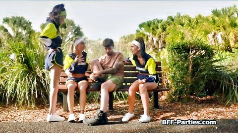 Four cheerleaders in skimpy uniforms tease guy on park bench outdoors