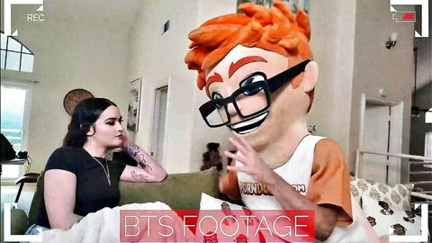 Remi Raw in BTS footage with orange mascot costume on couch