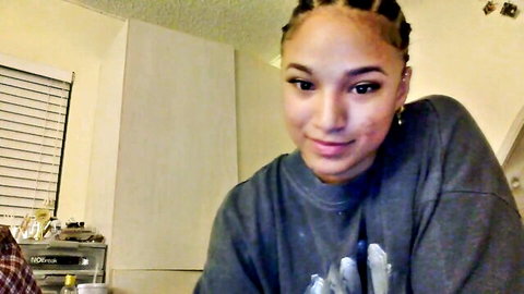 Ebony woman with braids smiling closeup in gray hoodie webcam selfie