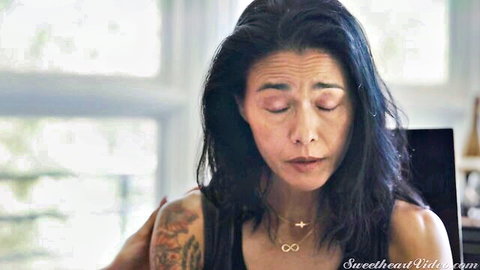 Tattooed Asian MILF with intense emotional expression as hand grips her bare shoulder