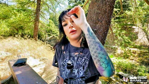 Tattooed brunette teen seductively posing outdoors in ripped tank top