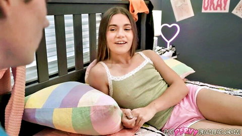 Skinny brunette teen in lace tank top and pink shorts smiles lying on bed with guy