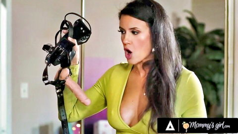 Penny Barber in green dress holding strap-on dildo, surprised expression in threesome tease