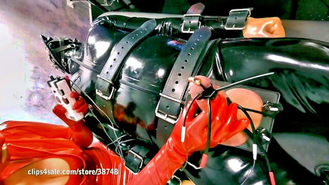 Femdom mistress in red latex dominates bound loser in black rubber BDSM sack