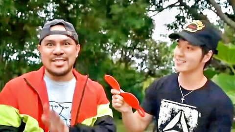 Two smiling Asian men outdoors, one holding red prop in casual jackets