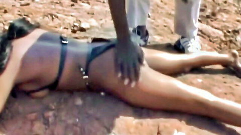Submissive African woman in BDSM harness gets spanked on her exposed ass while lying down