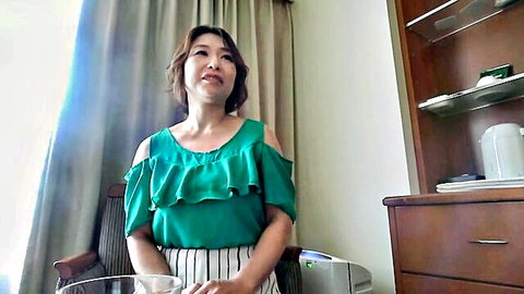 Mature Asian woman in 40s, green off-shoulder top, white striped pants, smiling seductively