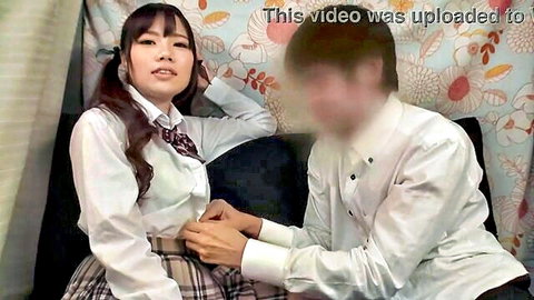 Japanese schoolgirl in uniform teased by blurred male friend on couch, suggestive touch