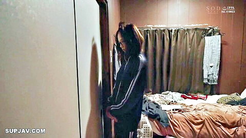 Japanese babe in tracksuit standing in bedroom with messy bed behind her