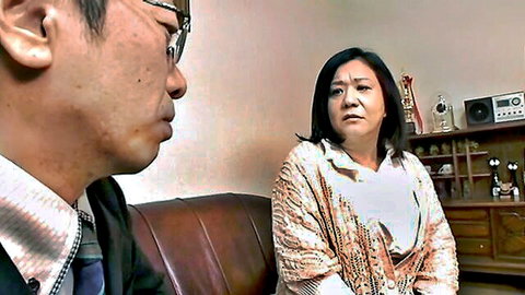 Asian man in suit talking seriously to mature Asian woman on leather couch in office