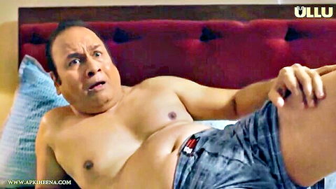 Shirtless mature Indian man with shocked expression lying on bed with low pants exposing waistband
