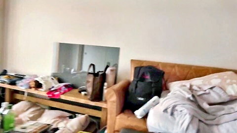 Messy bedroom shelf cluttered with clothes bags shoes and brown couch with blankets