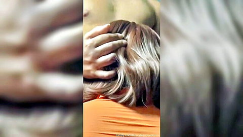 Man grips blonde woman's hair from behind while she wears orange top